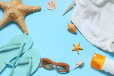 Mavi arka planda deniz kabukları, havlu ve bir şişe güneş kremi olan şık parmak arası terliklerden yapılmış çerçeve.
