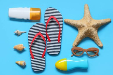 Şık çizgili terlikler, deniz kabukları, güneş gözlükleri, denizyıldızı ve mavi arka planda güneş kremi şişeleri.