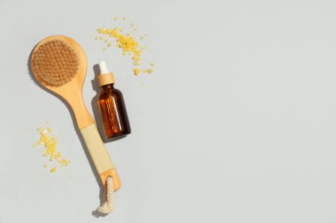 Bir şişe yağ, masaj fırçası ve gri arka planda deniz tuzu.