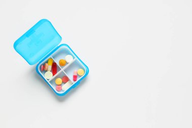 Beyaz arka planda haplar olan mavi plastik bir kap. Üst görünüm
