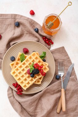 Farklı taze böğürtlenli Belçika waffle tabağı ve beyaz arka planda bir kavanoz bal.