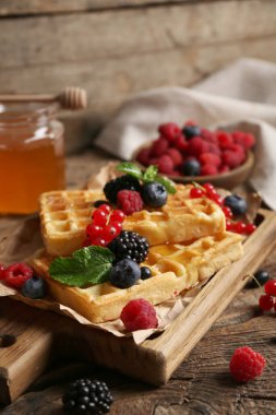 Farklı taze böğürtlen ve ahşap arka planda bal dolu Belçika waffle 'ları.