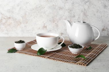 Beyaz zemin üzerinde kurumuş yapraklar olan çay fincanı ve çaydanlığı.