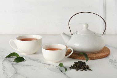 Beyaz arka planda kurumuş yapraklı çay fincanları ve çaydanlık.