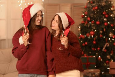Noel arifesinde evde şampanya kadehleriyle Noel Baba şapkalı genç lezbiyen çift.