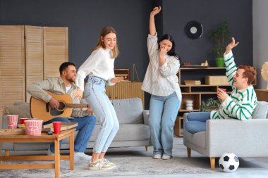 Dans eden arkadaşlarıyla evde gitar çalan genç bir adam.