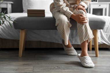 Yatak odasında diz ağrısı çeken genç bir kadın.