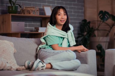 Genç Asyalı kadın akşam oturma odasında dinleniyor.