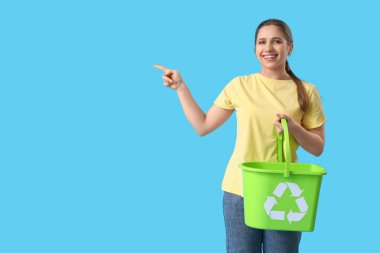 Geri dönüşüm kutusuyla mavi arka plandaki bir şeyi gösteren genç bir kadın. Atık sıralama kavramı
