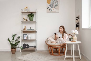 Oturma odasında koltukta otururken cep telefonu kullanan güzel bir genç kadın.