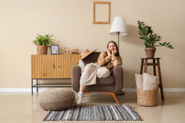 Oturma odasında koltukta otururken cep telefonuyla konuşan güzel bir genç kadın.