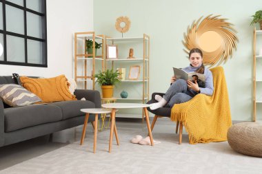 Oturma odasında koltukta oturmuş dergi okuyan güzel bir genç kadın.