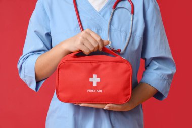 Kırmızı arka planda ilk yardım çantası olan kadın doktor.