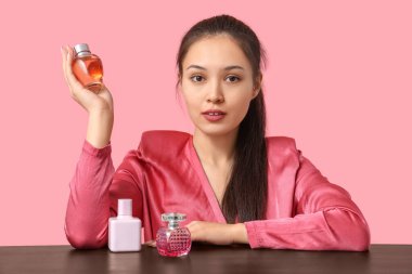 Masada pembe arka planda parfüm şişeleriyle güzel bir Asyalı kadın.