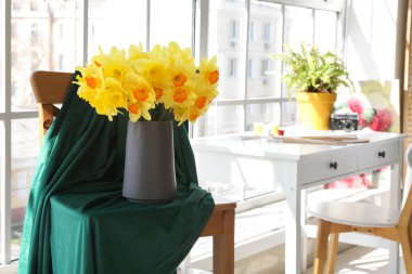 Nergis çiçekleri vazoda sandalyede, kumaş da oturma odasında.