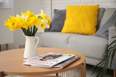 Oturma odasındaki vazoda nergis çiçekleri olan ahşap sehpa.