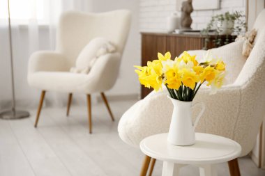 Oturma odasının içinde nergis çiçekleri olan rahat koltuklar ve kahve masası.