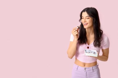 Pembe arka planda bir kutu lezzetli çikolata şekeri olan mutlu genç bir kadın.