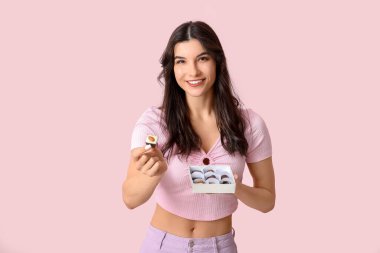 Pembe arka planda bir kutu lezzetli çikolata şekeri olan mutlu genç bir kadın.