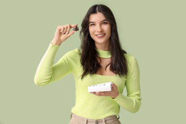 Yeşil arka planda çikolata yiyen güzel genç bir kadın.