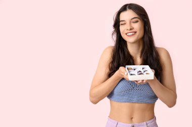 Güzel genç bir kadın pembe arka planda çikolata yiyor.