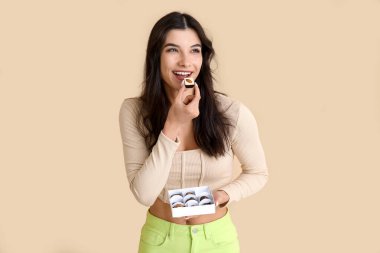 Bej arka planda bir kutu lezzetli çikolata şekeri olan genç bir kadın.