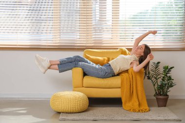 Genç bir kadın yastıklarla ve odada ekoseyle koltuğa uzanıyor.