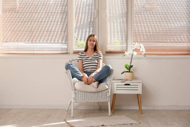 Orkide çiçeğinin yanındaki koltukta oturan genç kadın.