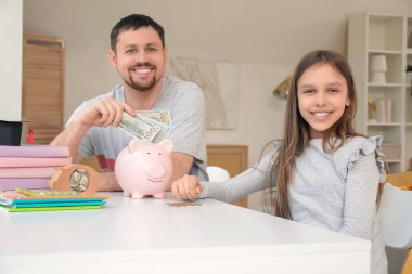 Babası ve kızı evdeki domuz kumbarasına para yatırıyor. Okul harcı konsepti