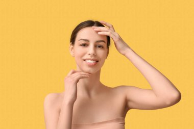 Sarı arka planda sağlıklı ciltli güzel, genç ve mutlu bir kadın.