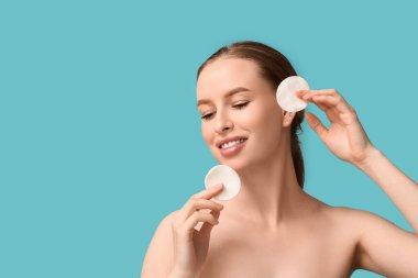 Sağlıklı cilt ve mavi arka planda pamuk pedleri olan güzel, mutlu bir kadın.