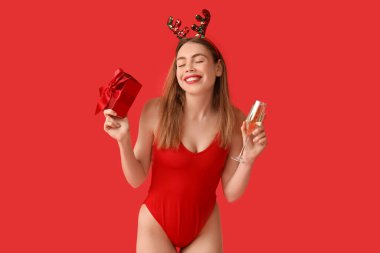 Mayo giymiş mutlu genç bir kadın ve kırmızı arka planda hediye kutusu olan bir kokteyl taşıyan ren geyiği boynuzları. Temmuz 'da Noel