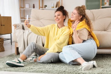 Genç kadınlar oturma odasında yerde selfie çekiyorlar.