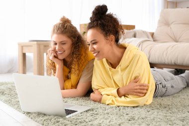 Genç kadınlar oturma odasında yerde dizüstü bilgisayar kullanıyorlar.