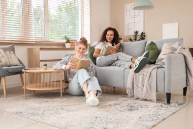 Oturma odasında kitap okuyan genç kadınlar