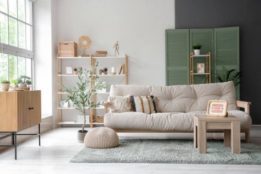 Yumuşak yastıklı kanepe, resimli sehpa ve oturma odasında dekoratif zeytin ağacı.