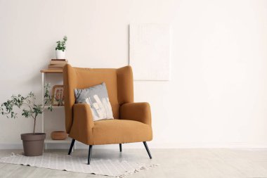 Yastıklı koltuk, kitaplı raf ünitesi ve oturma odasının iç tarafında dekoratif zeytin ağacı.