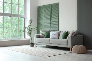 Yastıklı rahat bir kanepe, puf ve dekoratif zeytin ağacı.