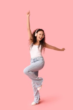 Pembe arka planda dans eden kulaklıklı mutlu Afro-Amerikan kadın.