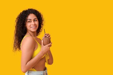 Sarı arka planda taze hindistan cevizi ve samanla güzel bir Afro-Amerikalı kadın.