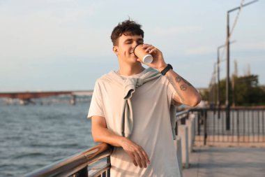 Yakışıklı genç adam rıhtımda nefis latte içiyor.