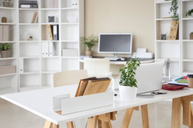 Interior of stylish office with workplaces, laptop and shelving unit clipart