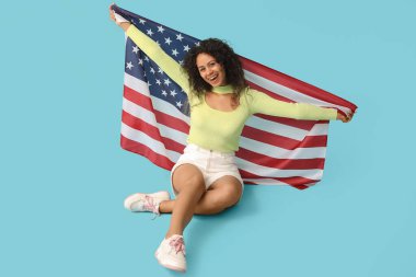 Mavi arka planda oturan mutlu Afro-Amerikalı kadın.