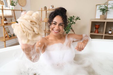 Güzel, genç, mutlu, Afro-Amerikan bir kadın evde sünger ve sabun köpüğüyle banyo yapıyor.