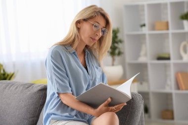 Evde kitap okuyan güzel olgun kadın portresi.