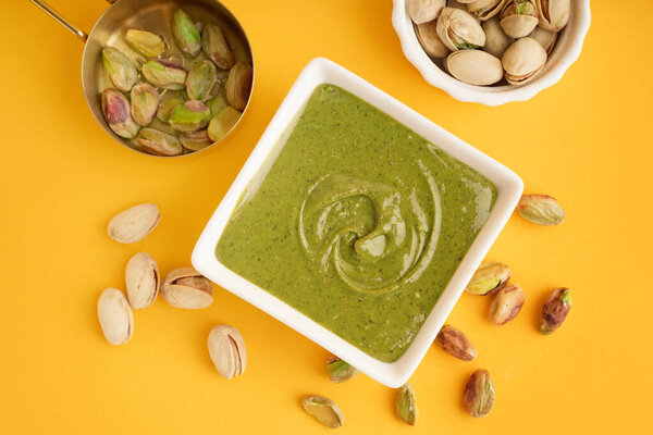 Вкусная фисташковая паста в миске и измерительная чашка на желтом фоне