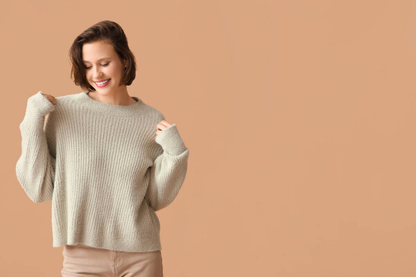 Красивая молодая женщина в стильном сером свитере на коричневом фоне