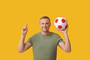 Futbol topu olan yakışıklı olgun bir adam sarı arka plandaki bir şeyi işaret ediyor.