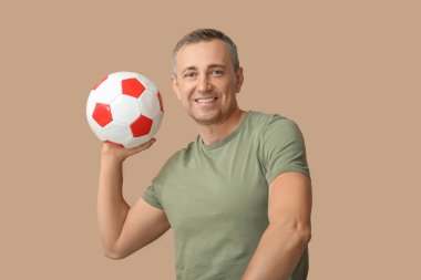 Kahverengi arka planda futbol topuyla oynayan yakışıklı olgun bir adam.