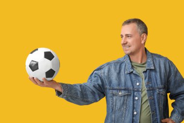Sarı arka planda futbol topu olan yakışıklı olgun bir adam.